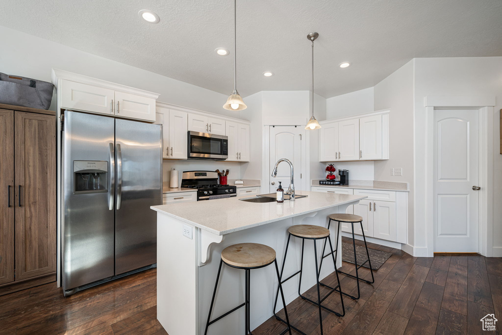 Kitchen featuring light countertops, a sink, stainless steel appliances, a breakfast bar area, and dark wood-style floors
