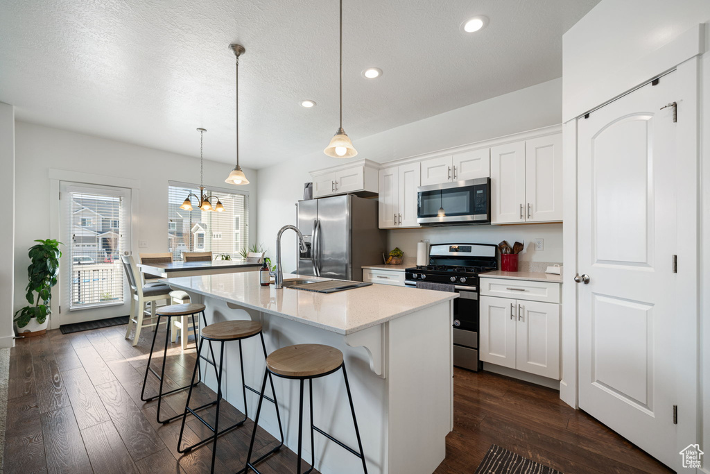Kitchen with stainless steel appliances, dark wood-style floors, a kitchen breakfast bar, and a chandelier