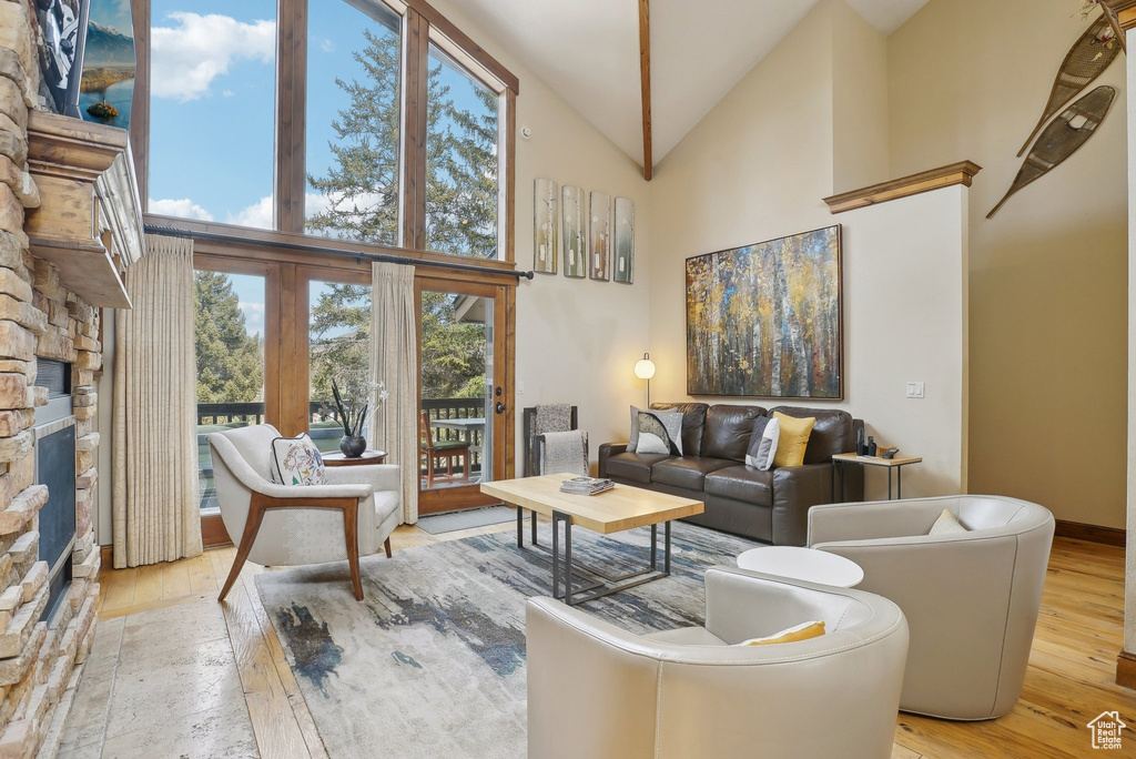 Living room with a stone fireplace, high vaulted ceiling, hardwood / wood-style flooring, and baseboards