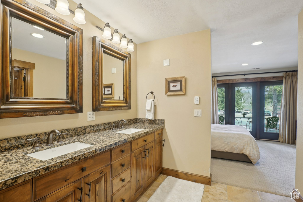 Ensuite bathroom with recessed lighting, double vanity, baseboards, and a sink