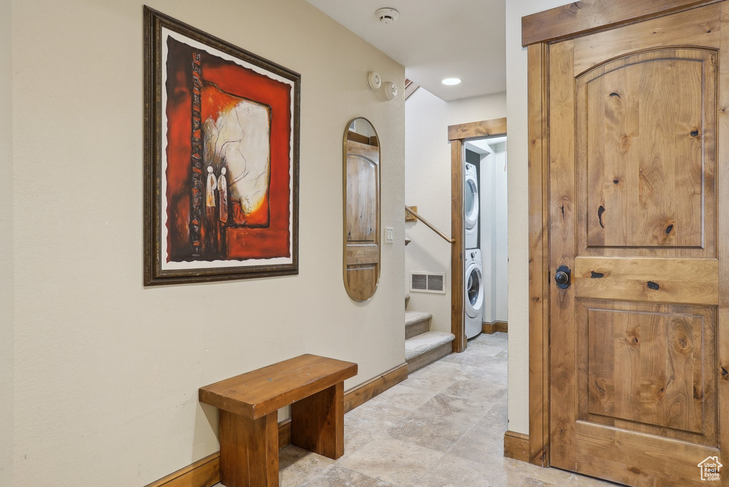 Hall with stairway, stacked washer / dryer, baseboards, and visible vents