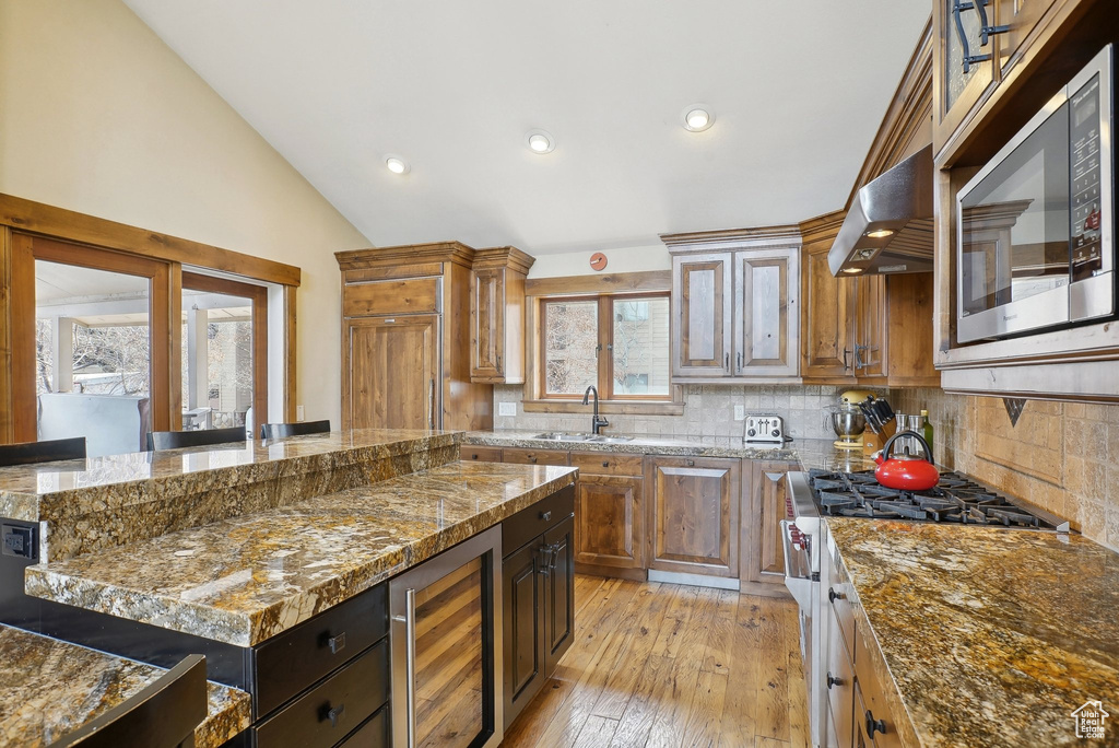 Kitchen featuring backsplash, beverage cooler, vaulted ceiling, and stainless steel appliances