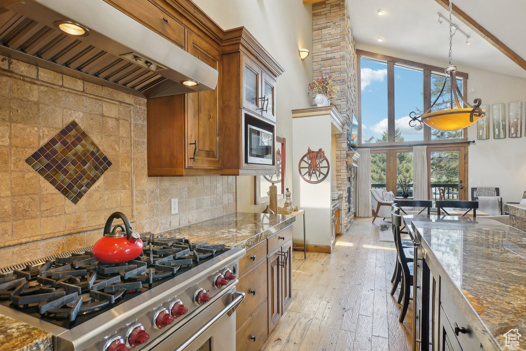 Kitchen featuring custom exhaust hood, tasteful backsplash, brown cabinets, light wood finished floors, and stainless steel appliances