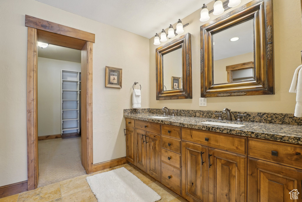 Bathroom featuring a sink, a walk in closet, baseboards, and double vanity