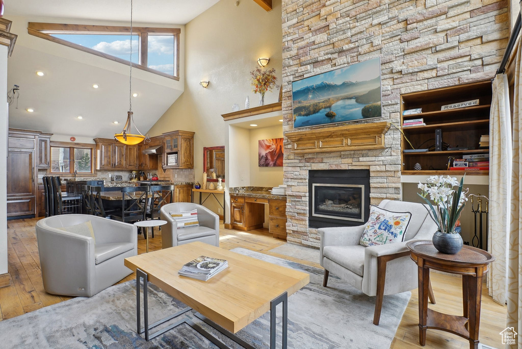 Living area with a stone fireplace, light wood-style flooring, a towering ceiling, and a healthy amount of sunlight