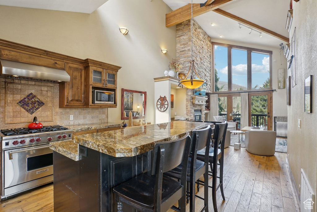 Kitchen featuring tasteful backsplash, ventilation hood, brown cabinetry, stainless steel appliances, and a breakfast bar area