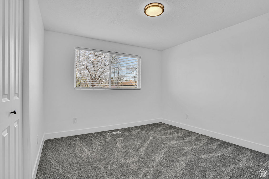 Spare room with dark carpet, baseboards, and a textured ceiling