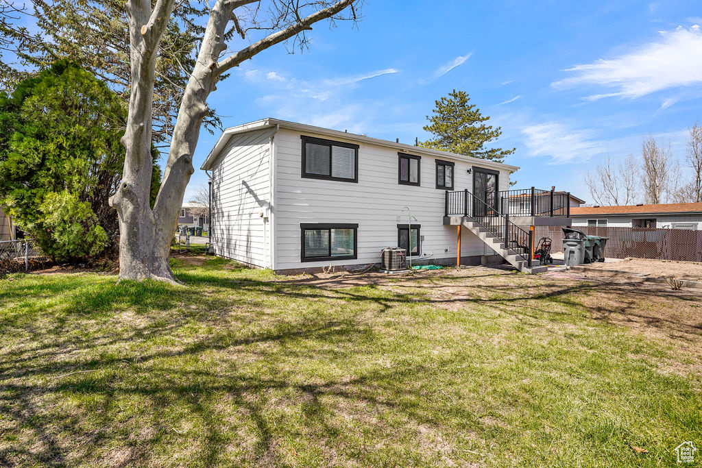 Back of property featuring a yard, fence, central AC unit, and stairs