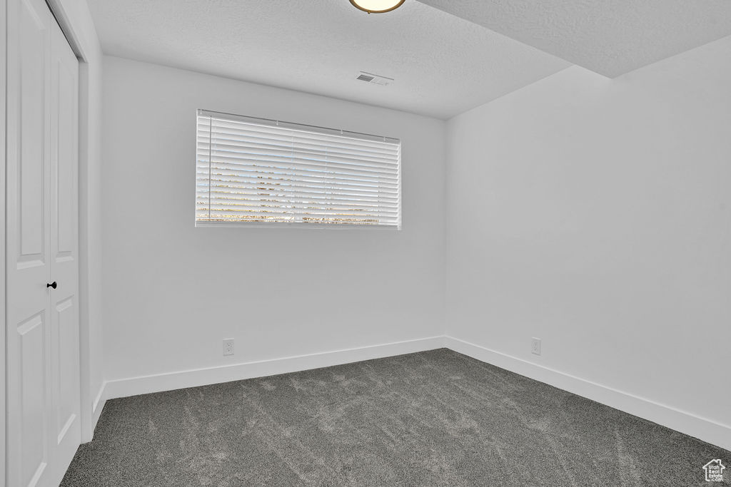 Unfurnished room with dark carpet, baseboards, visible vents, and a textured ceiling