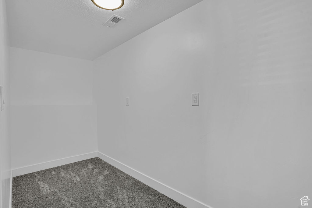 Spare room featuring dark carpet, a textured ceiling, baseboards, and visible vents