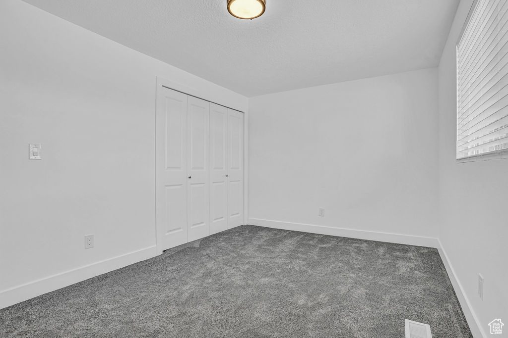 Unfurnished bedroom featuring visible vents, baseboards, a closet, dark carpet, and a textured ceiling