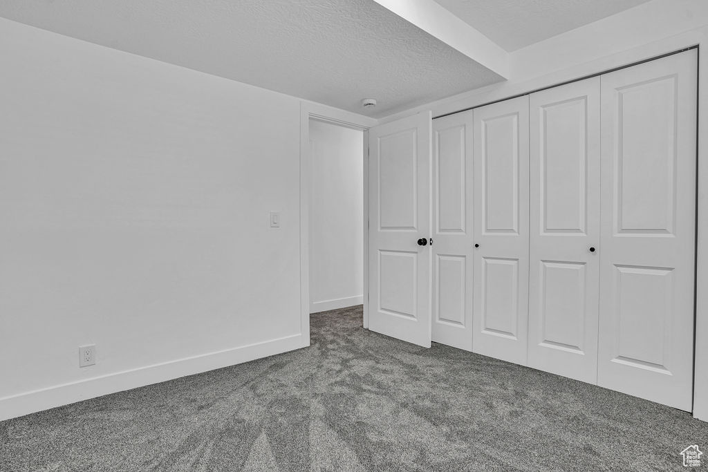 Unfurnished bedroom with a textured ceiling, a closet, baseboards, and carpet