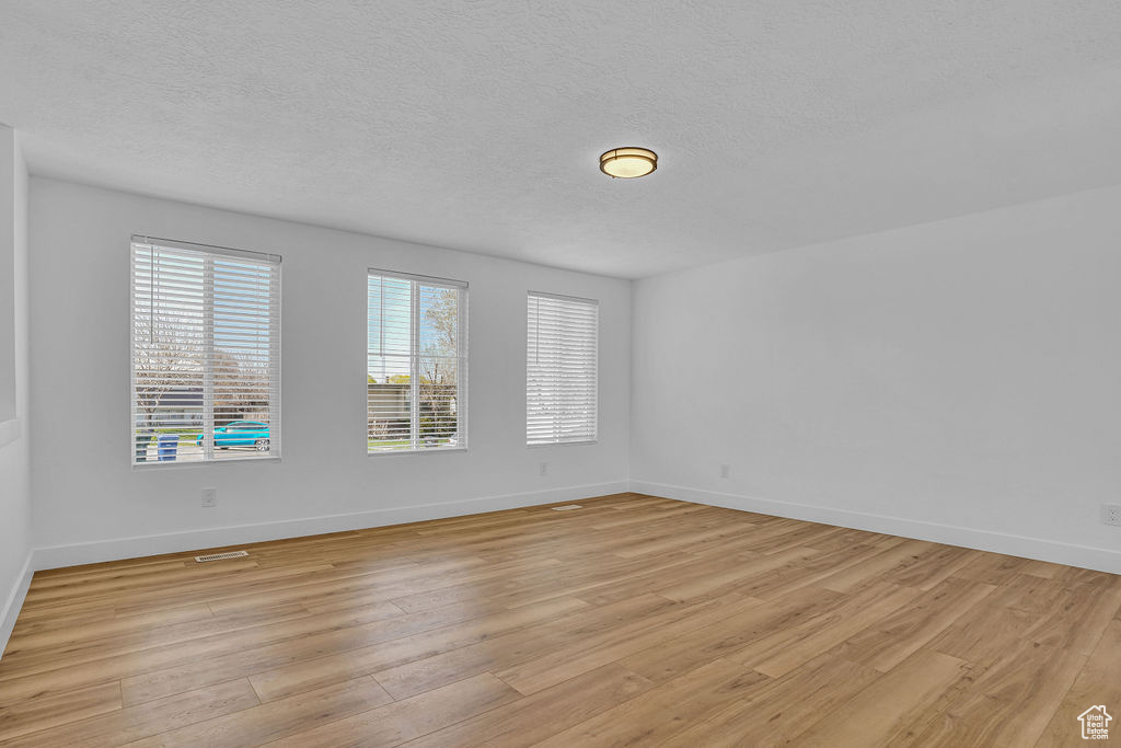 Unfurnished room featuring light wood-style floors, baseboards, and a textured ceiling
