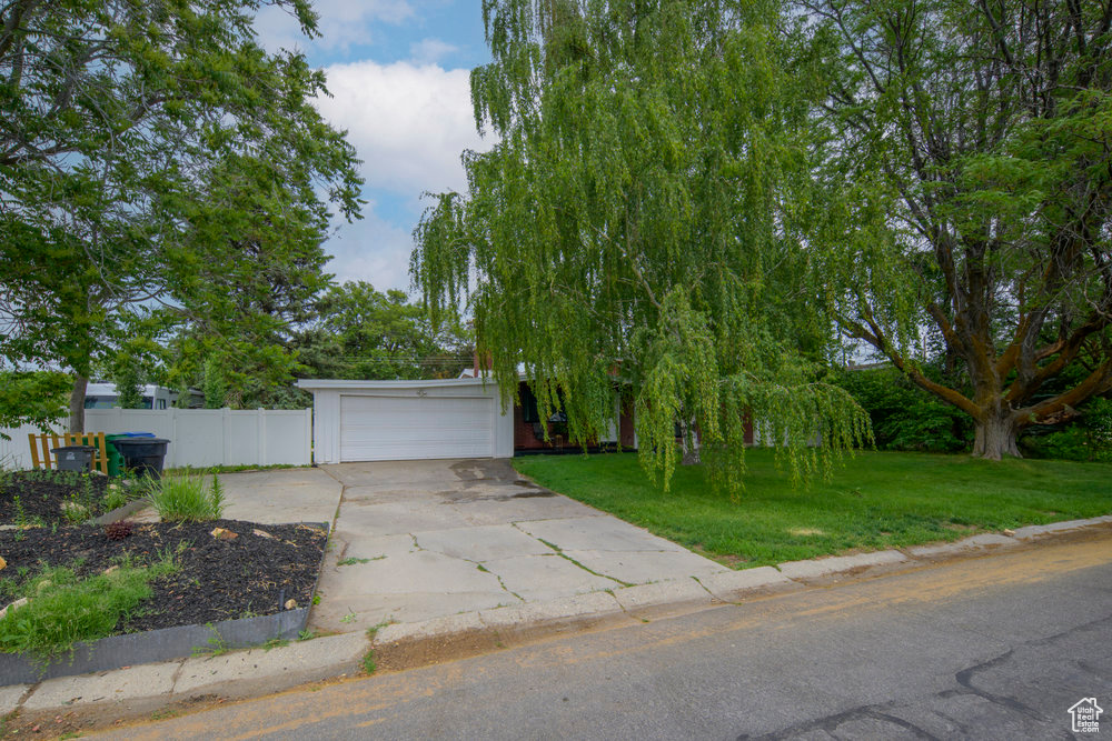 View of property hidden behind natural elements featuring driveway and an attached garage
