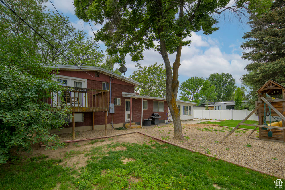 Rear view of house with a playground, brick siding, and a wooden deck