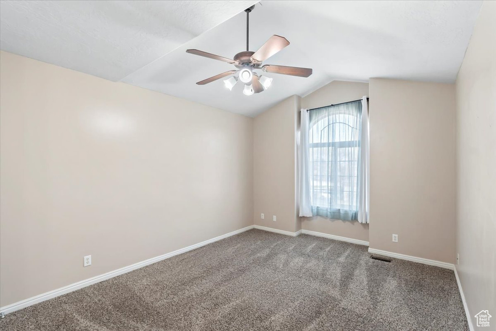 Carpeted spare room featuring visible vents, baseboards, a ceiling fan, and lofted ceiling