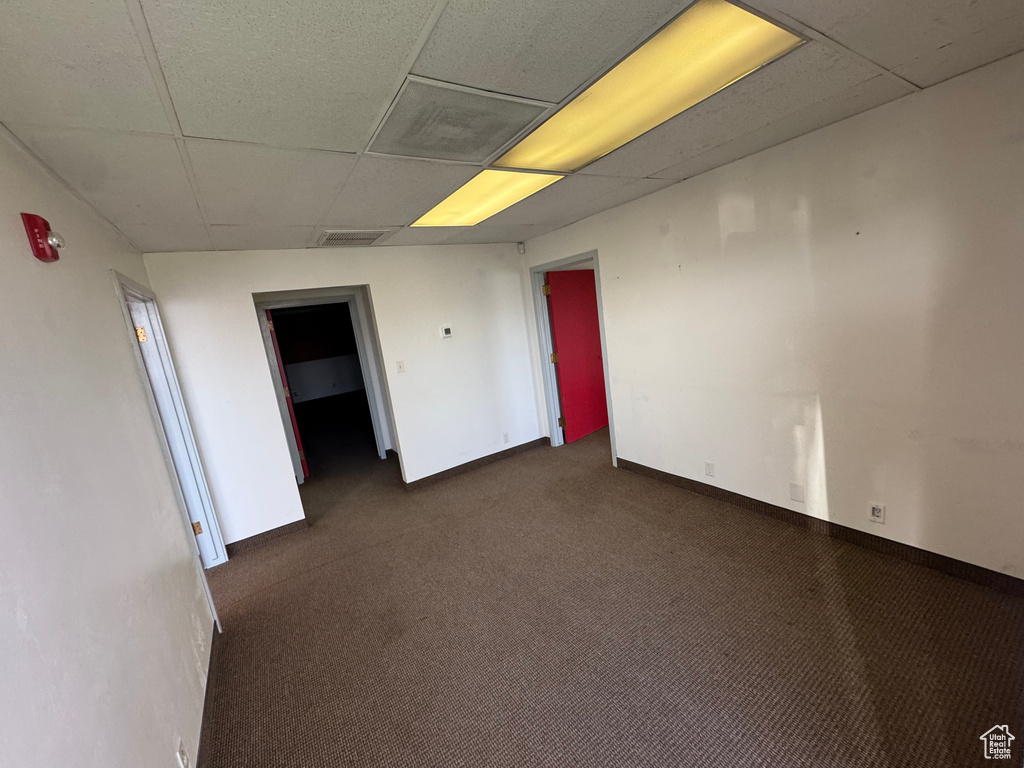 Empty room featuring a paneled ceiling, visible vents, dark colored carpet, and baseboards