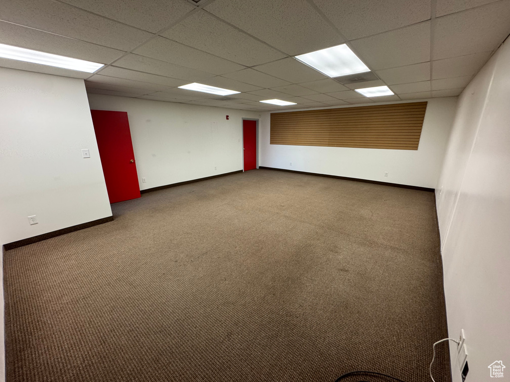 Carpeted empty room featuring baseboards and a drop ceiling