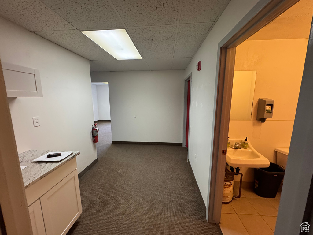 Corridor with carpet flooring, a paneled ceiling, baseboards, and a sink