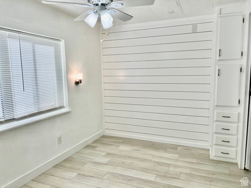 Unfurnished room featuring light wood-type flooring, wooden walls, baseboards, and a ceiling fan
