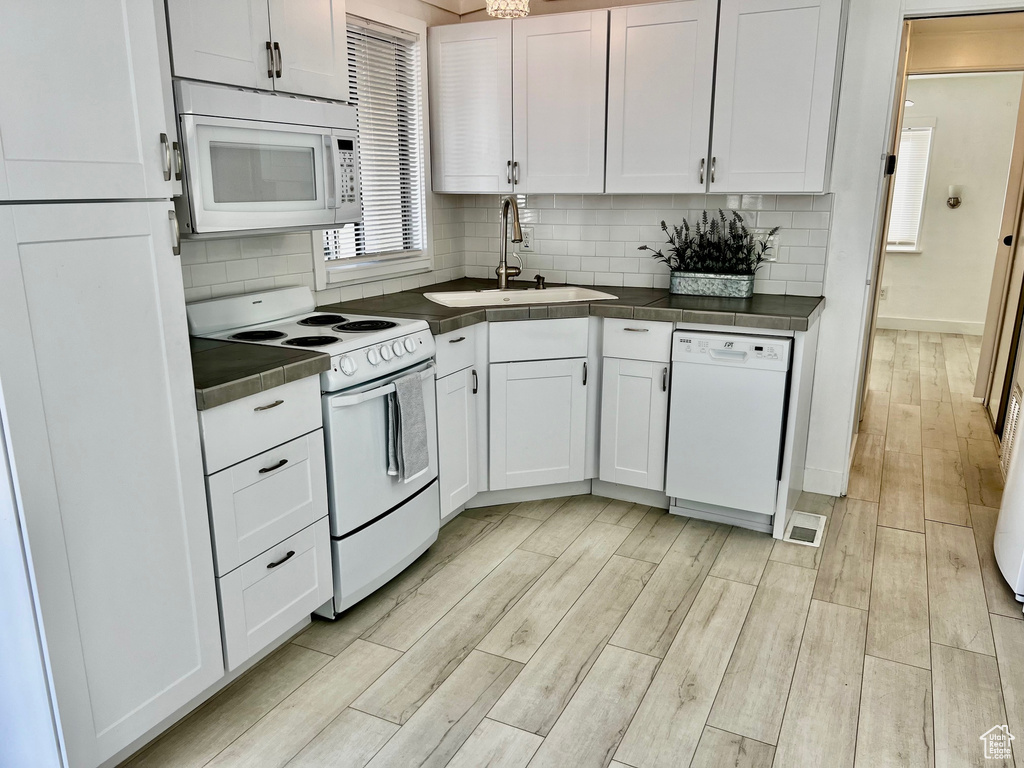 Kitchen with a sink, dark countertops, white appliances, white cabinetry, and wood finish floors