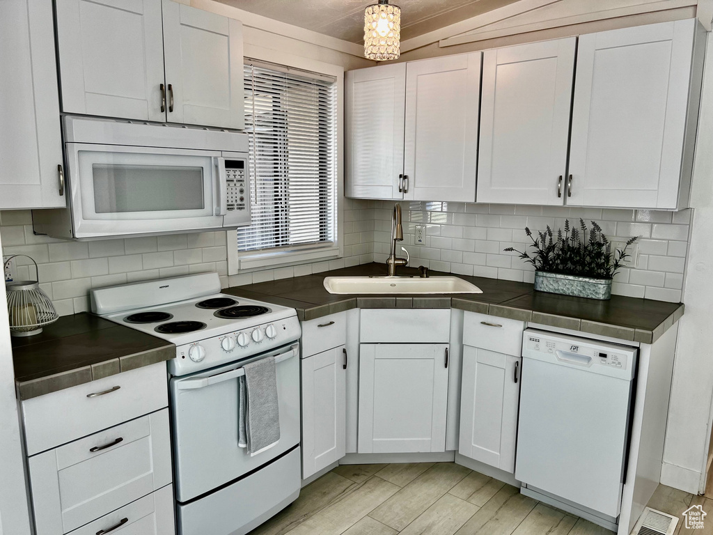 Kitchen featuring tasteful backsplash, white cabinets, a sink, light wood-type flooring, and white appliances