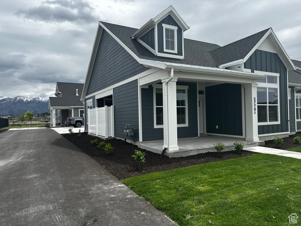 View of front of property featuring covered porch, board and batten siding, a shingled roof, a front yard, and a mountain view