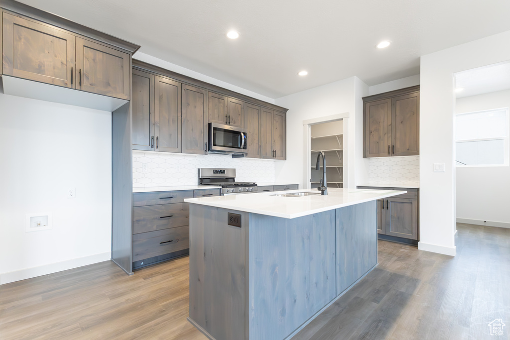Kitchen featuring an island with sink, light countertops, stainless steel appliances, light wood finished floors, and a sink