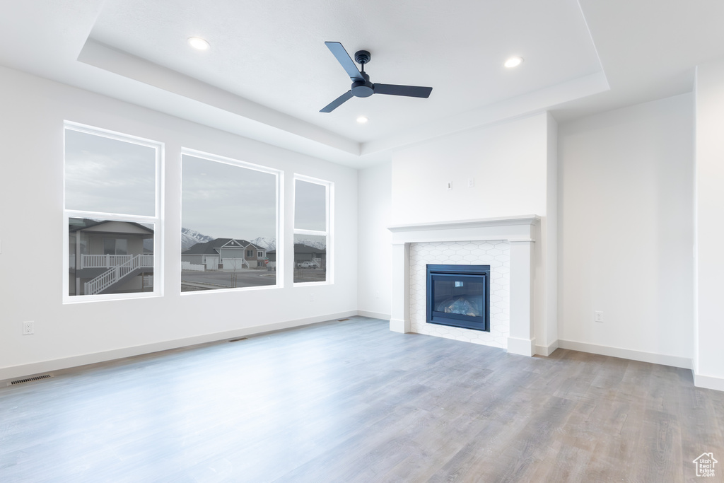 Unfurnished living room featuring visible vents, a tray ceiling, a ceiling fan, and wood finished floors