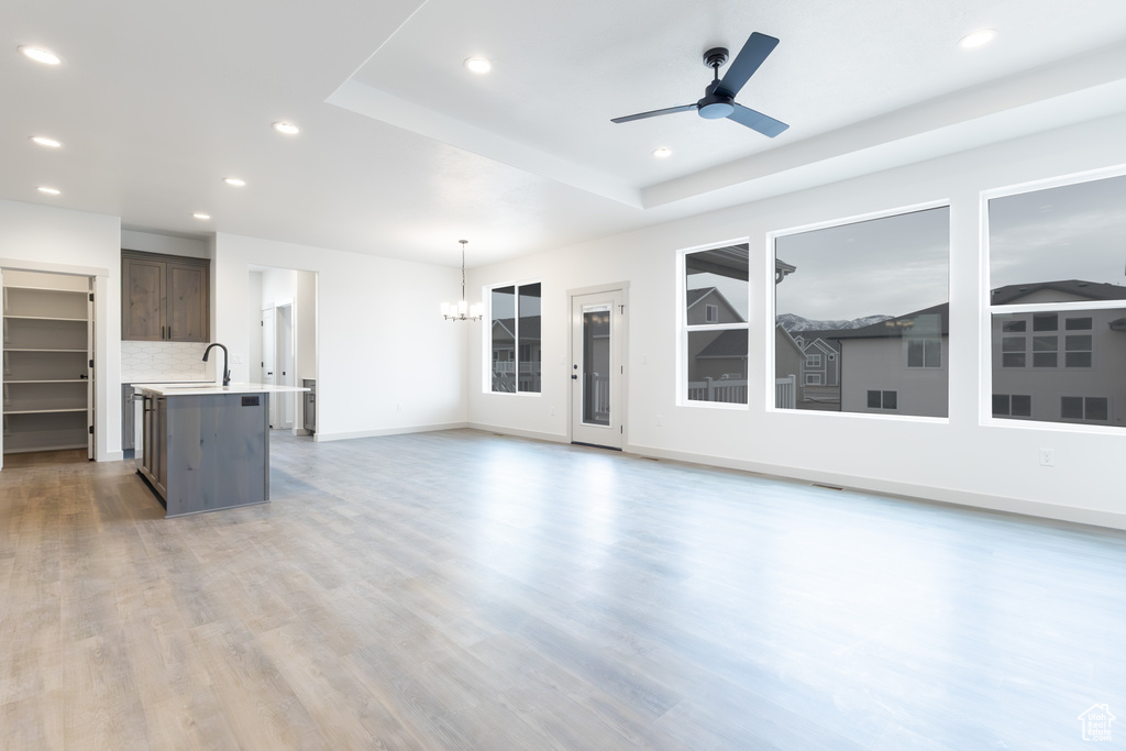 Unfurnished living room with baseboards, recessed lighting, light wood-style floors, ceiling fan with notable chandelier, and a sink