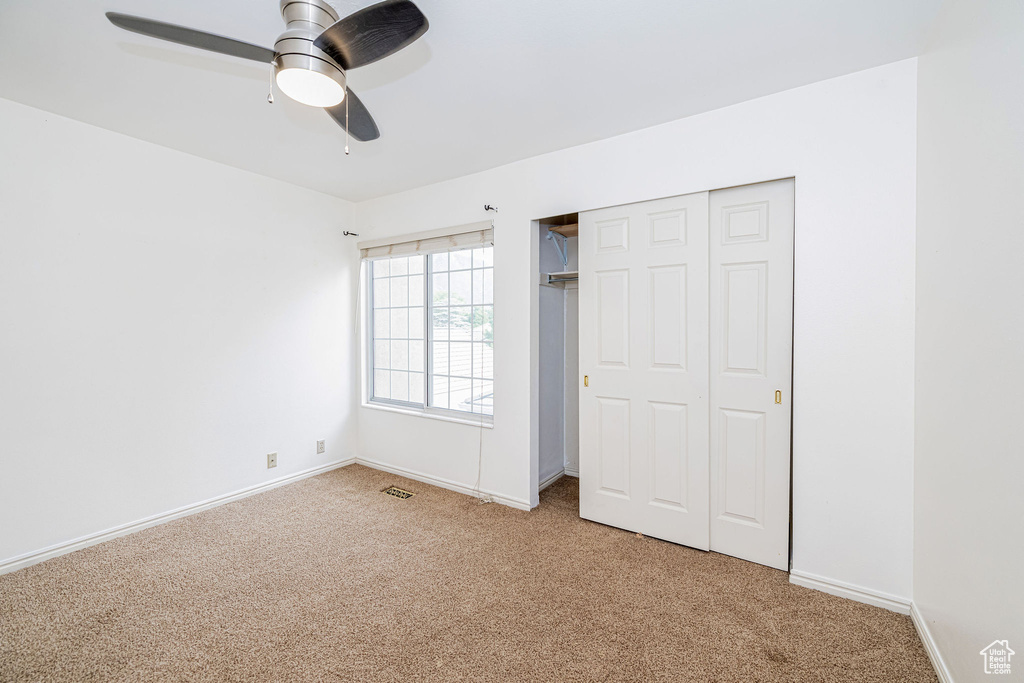 Unfurnished bedroom featuring light colored carpet, a closet, and ceiling fan