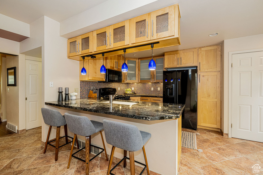 Kitchen featuring black appliances, a peninsula, backsplash, glass insert cabinets, and dark stone countertops