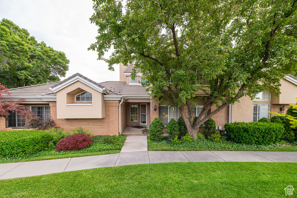 View of front of property with a front yard, brick siding, a tile roof, and stucco siding