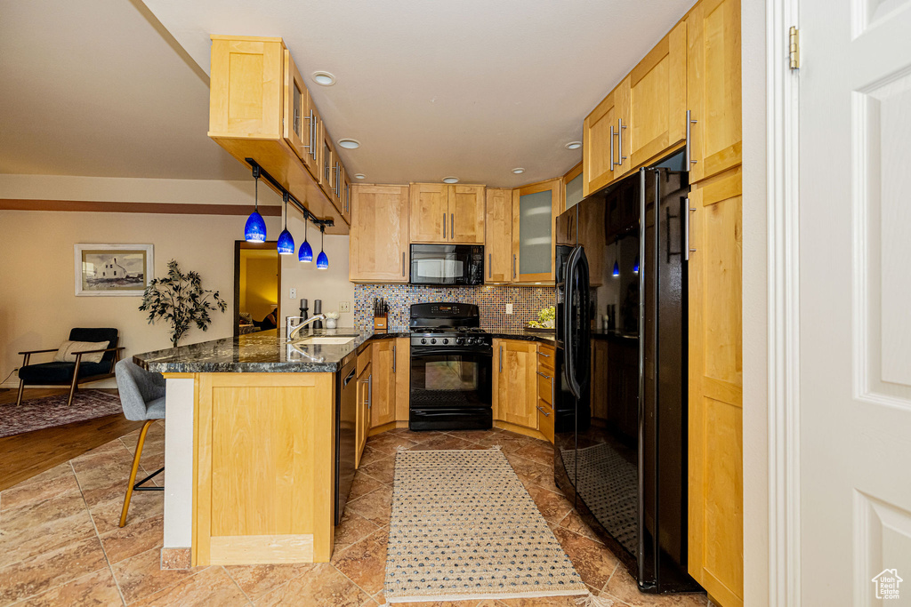 Kitchen featuring black appliances, a peninsula, a breakfast bar, decorative backsplash, and glass insert cabinets