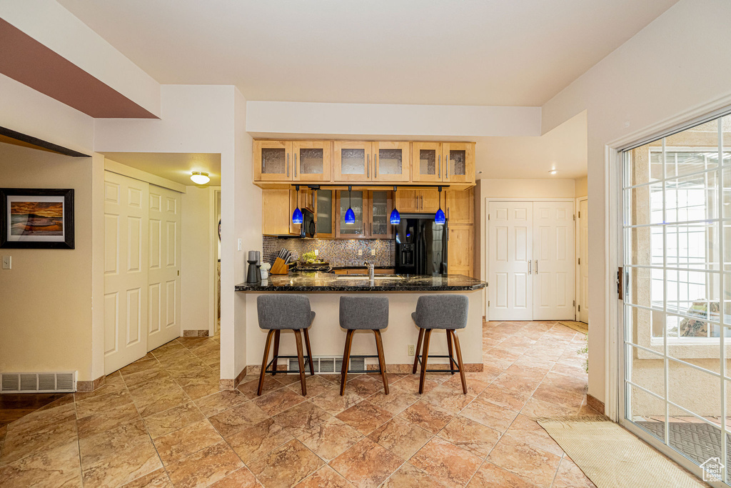 Kitchen with black fridge, a kitchen bar, tasteful backsplash, a peninsula, and light stone finish flooring