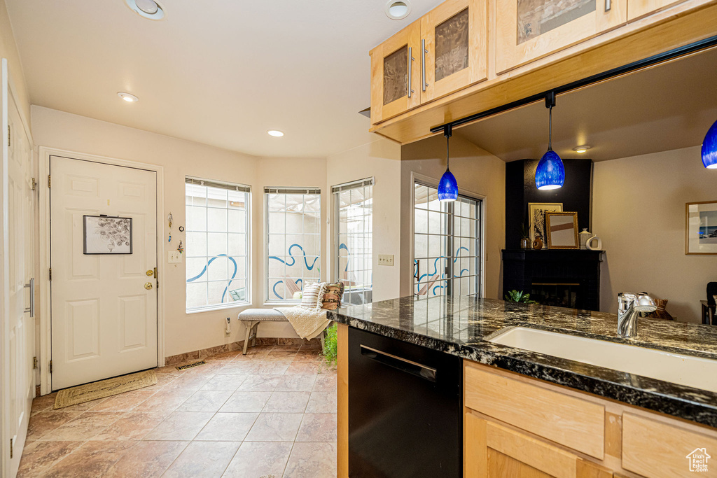 Kitchen with black dishwasher, glass insert cabinets, light brown cabinets, recessed lighting, and hanging light fixtures
