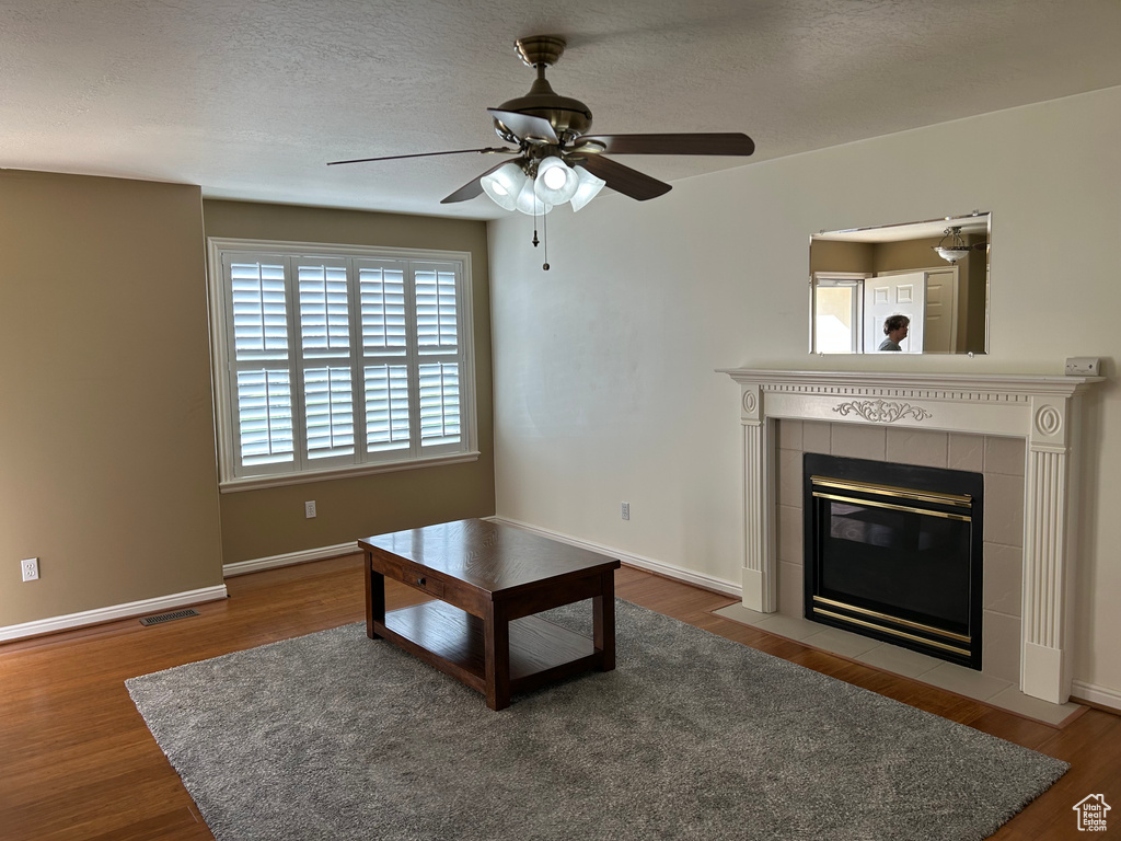Unfurnished living room with a textured ceiling, visible vents, ceiling fan, a tile fireplace, and wood finished floors