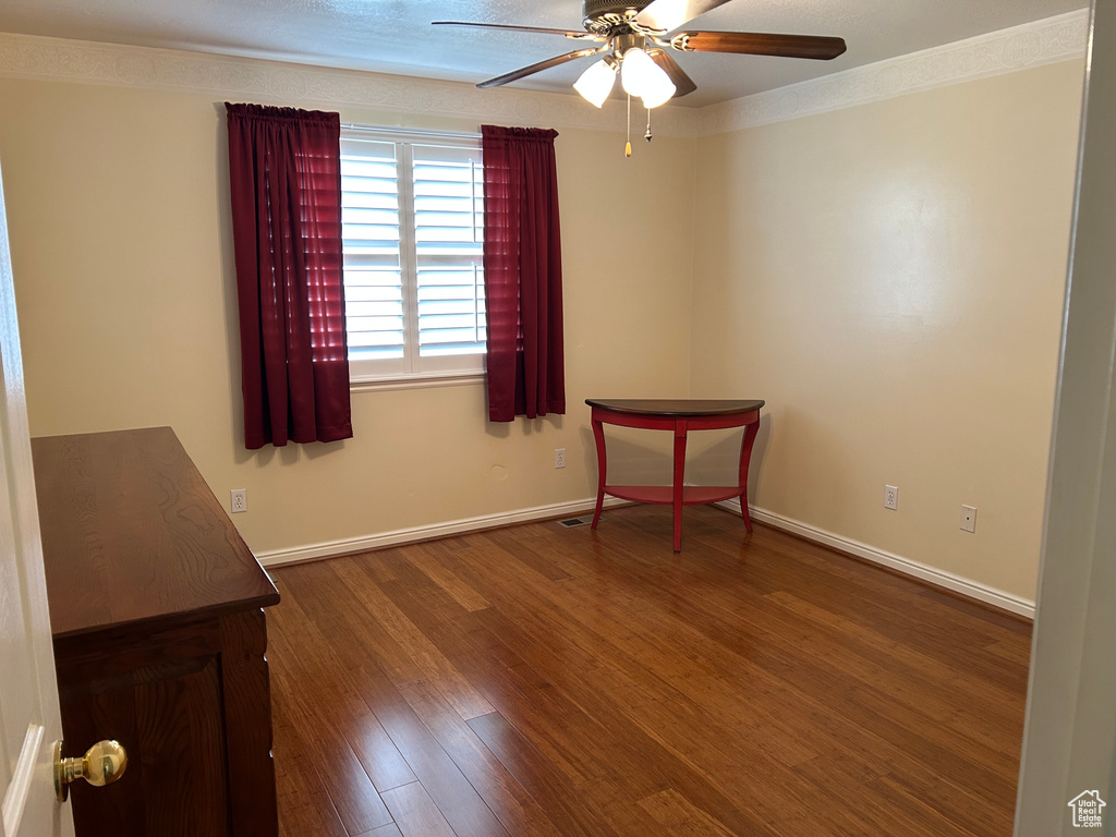 Empty room featuring wood finished floors, ornamental molding, baseboards, and a ceiling fan