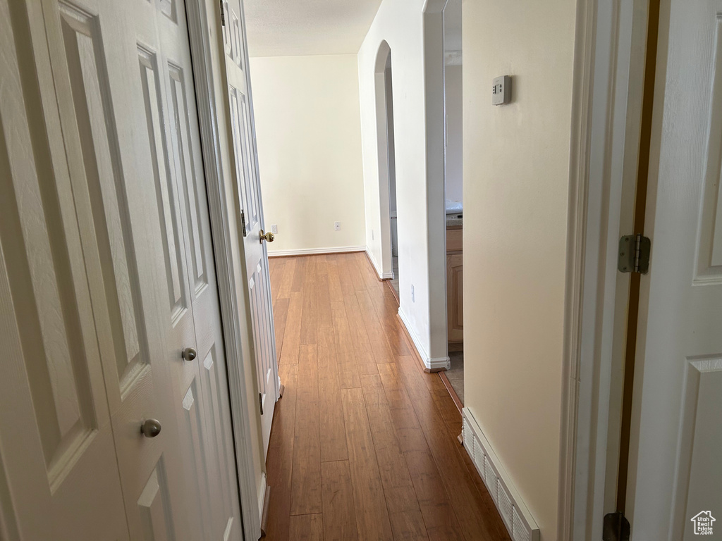 Hallway featuring visible vents, wood-type flooring, arched walkways, and baseboards