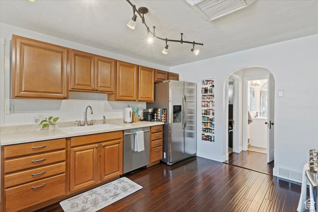 Kitchen with arched walkways, a sink, dark wood-style flooring, light countertops, and stainless steel appliances