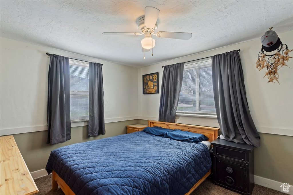 Carpeted bedroom with a textured ceiling, baseboards, and a ceiling fan