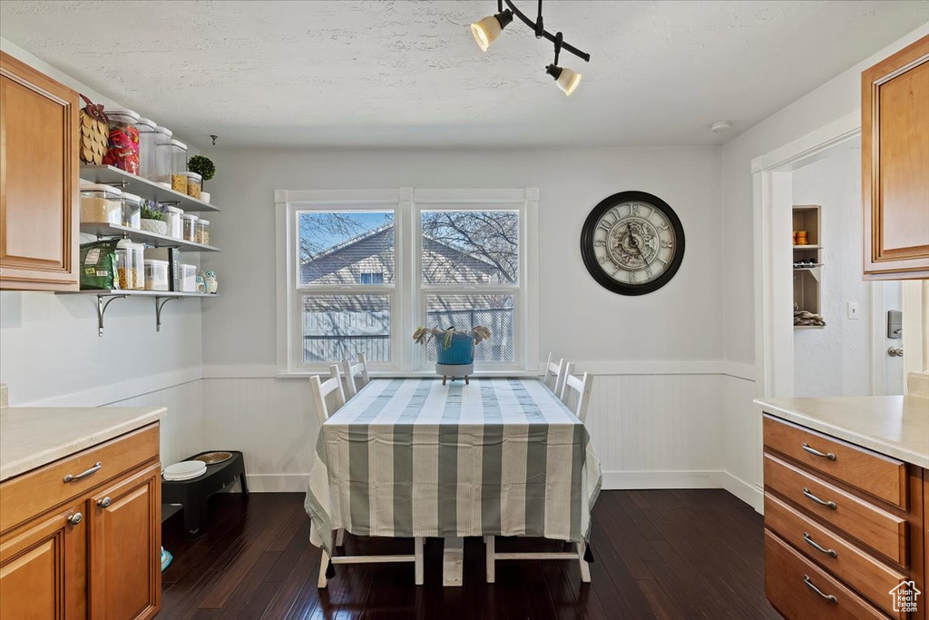Dining area with dark wood-type flooring, a textured ceiling, and a wainscoted wall
