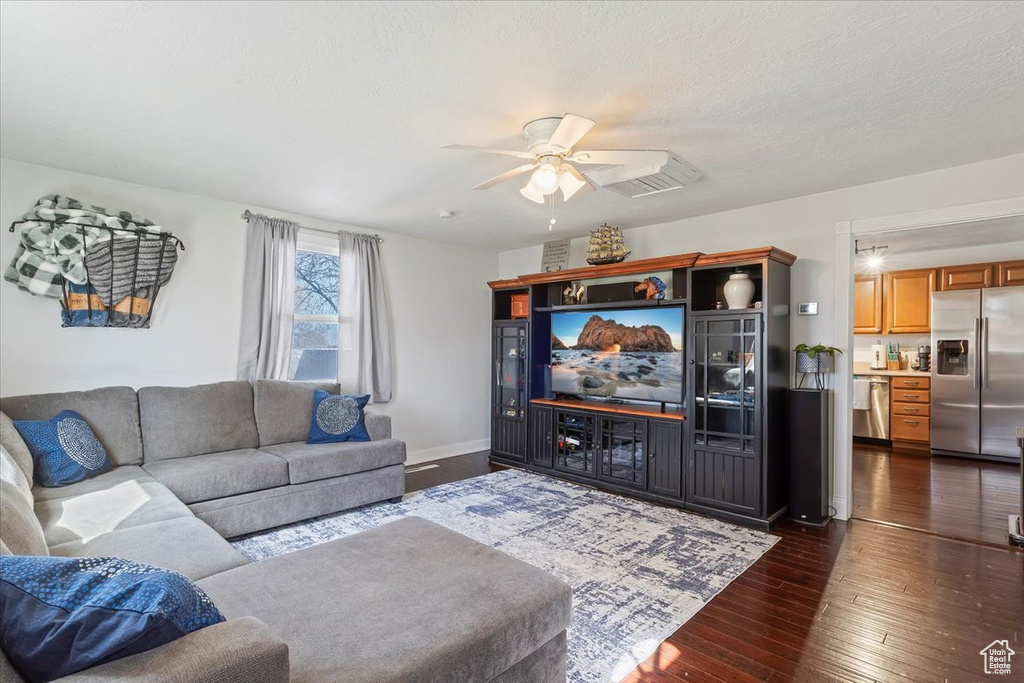 Living area featuring dark wood-style floors, a textured ceiling, baseboards, and ceiling fan