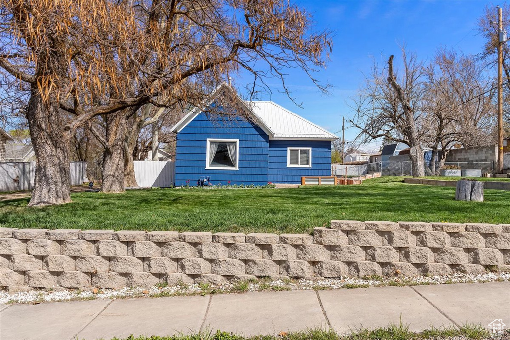 View of side of property with fence, metal roof, and a lawn