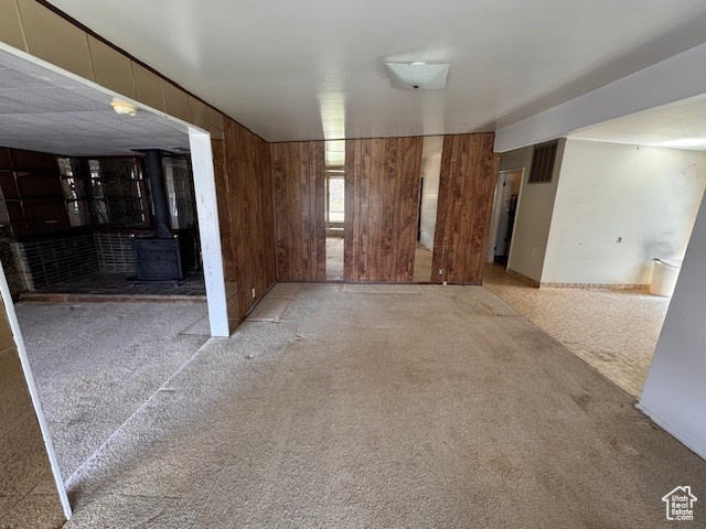 Carpeted spare room featuring wooden walls and a wood stove