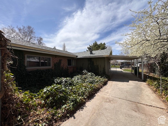 View of side of property featuring driveway, an attached carport, and brick siding