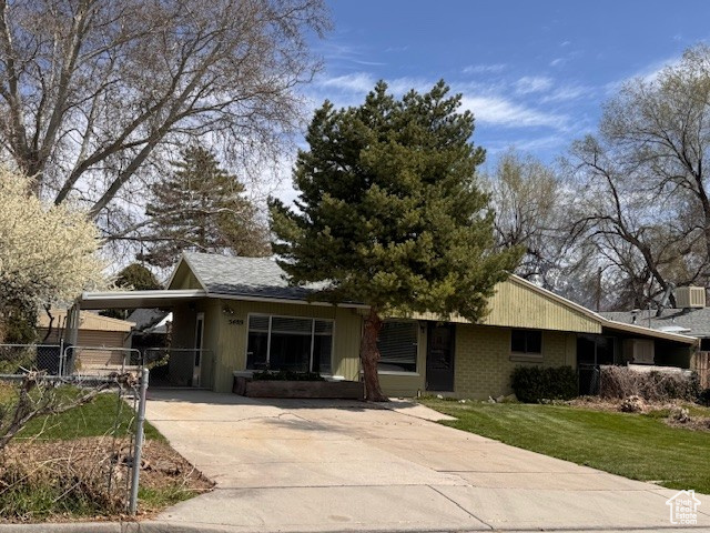 View of front of home featuring a front yard, fence, brick siding, an attached carport, and driveway