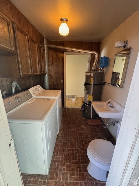 Laundry room featuring brick patterned floor, visible vents, water heater, a sink, and washer and clothes dryer