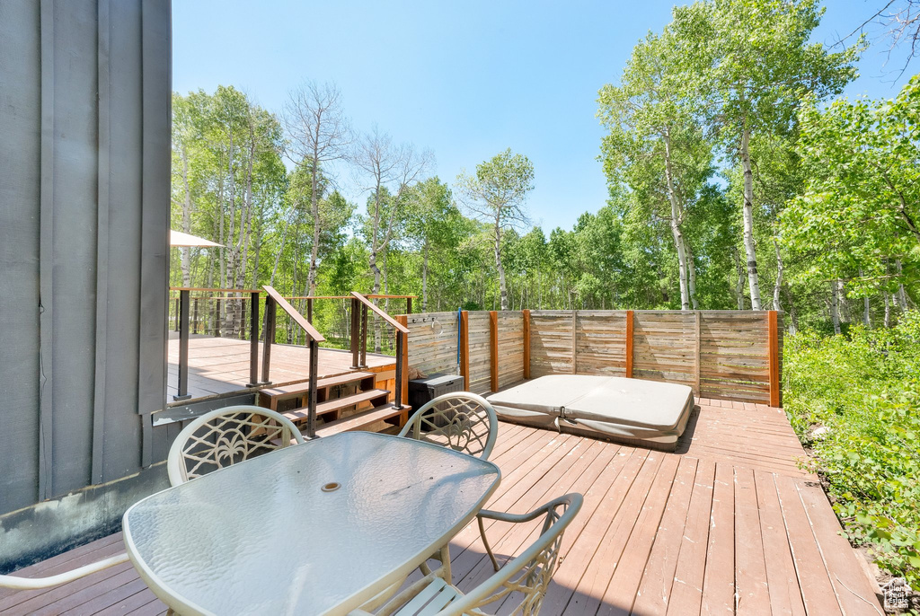 Wooden terrace featuring outdoor dining space and view of wooded area