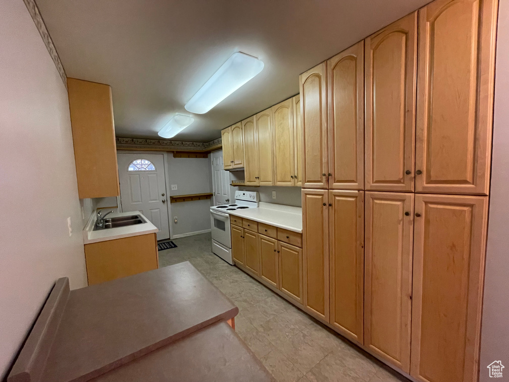 Kitchen featuring baseboards, light brown cabinets, a sink, light countertops, and white electric stove